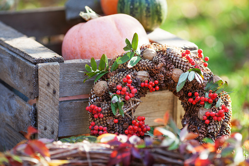 Wicker wreath decorated orange leaves, autumn berries and vegetables: pumpkins,  \nmountain ash, nuts, cones at the wooden background. Thanksgiving day.