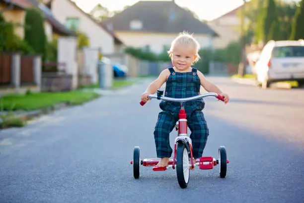 Cute toddler child, boy, playing with tricycle on the street, kid riding bike on sunset