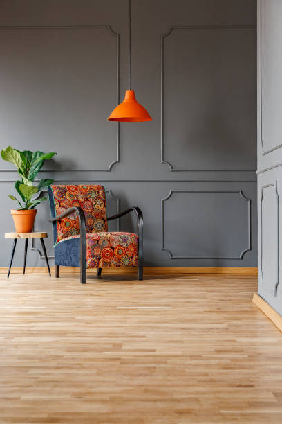 istock Plant on a wooden side table and a comfortable armchair with a boho style pattern in a gray living room interior and copy space place for a floor lamp. Real photo. 1036089218