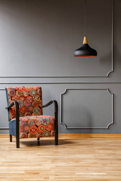 istock Vintage armchair with colorful, boho style pattern and a black ceiling light in a fancy, gray living room interior and copy space place for a cabinet. Real photo. 1036089228