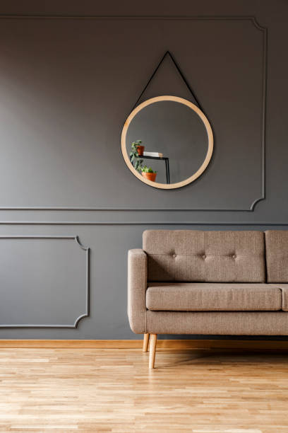 istock A round mirror above a simple, elegant brown sofa and a place for a side table in a fancy living room interior. Real photo. 1036092654