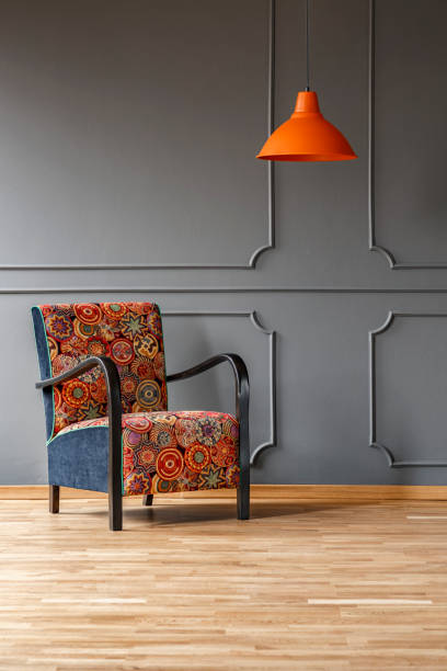 istock Vibrant orange ceiling light and a comfortable armchair with a colorful boho pattern in a gray living room interior with place for a table. Real photo. 1036092678