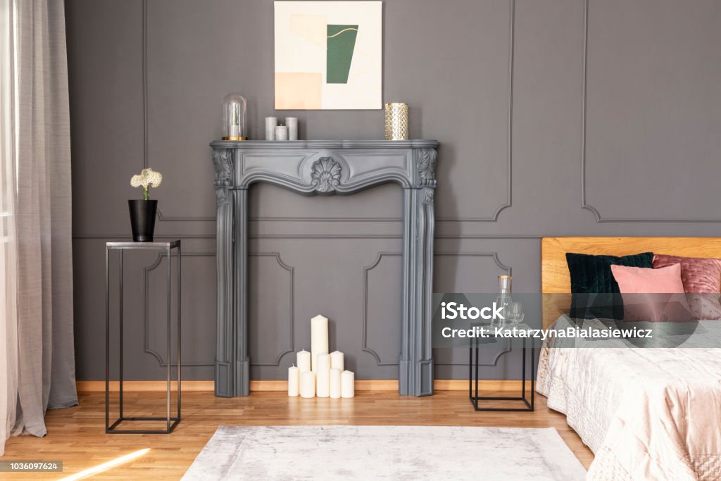 Elegant bedroom interior with a candles set in a fireplace portal, metal tables, wall molding and bed Artificial Stock Photo