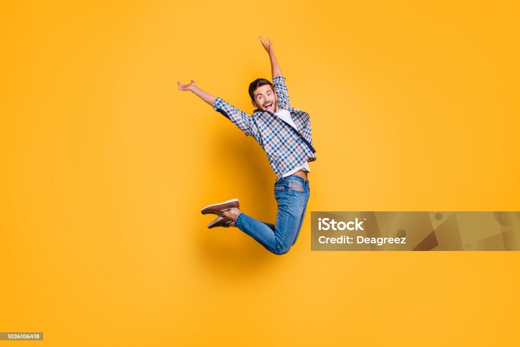 Full-body portrait of flying and cheerful man in sneakers, denim Full-body portrait of flying and cheerful man in sneakers, denim outfit, jumping with raised arms isolated on shine yellow background Jumping Stock Photo