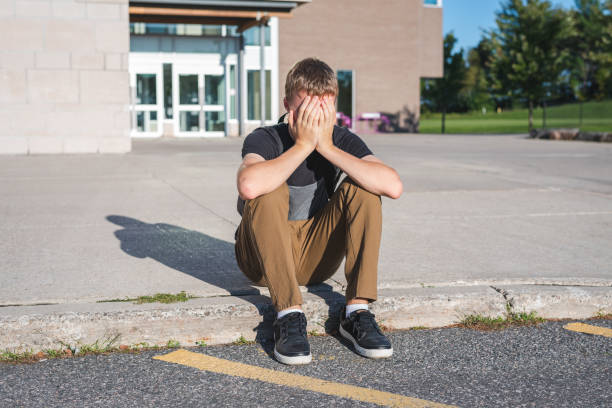 istock Sad teenage boy sitting on a curb while he covers his face with his hand. 1036111968
