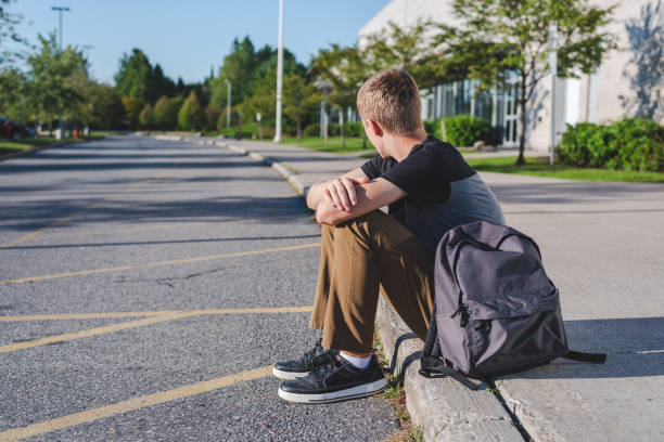 adolescente solitario sentado en la acera junto a la escuela secundaria. - one teenage fotografías e imágenes de stock