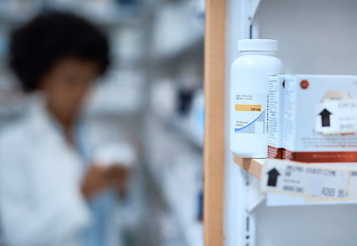 Shot of shelves stocked with various medicine in a chemist with a pharmacist blurred in the background