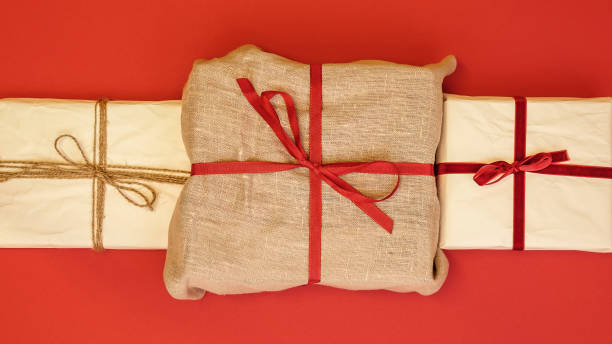 Christmas gift boxes on red background. Burlap canvas and reused wrapping paper Christmas gift boxes on red background. Burlap canvas and reused wrapping paper with red ribbon and linen string. linen flax textile burlap stock pictures, royalty-free photos & images