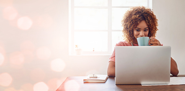 Cropped shot of a young female designer having coffee while working on her laptop against a digitally enhanced background