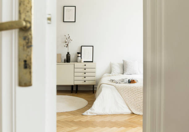 istock A peek through a half open door into a monochromatic beige and white bedroom interior with a bed and a drawer cabinet. Real photo. 1036143496
