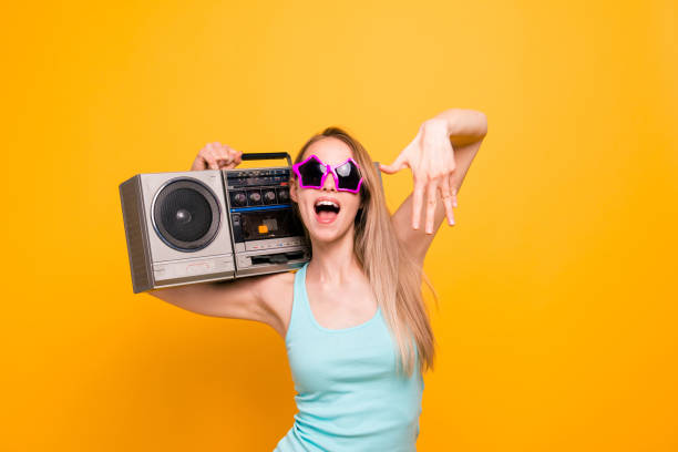 attraente bella bella ragazza bionda caucasica dai capelli lisci, che indossa camicia casual, occhiali da sole a forma di stella. tenere boom box, godersi la musica. isolato su sfondo giallo - music women disco joy foto e immagini stock