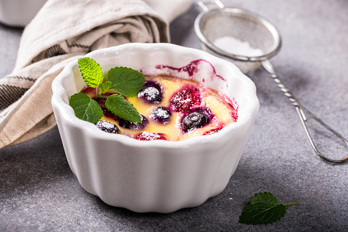 Berry clafouti. Traditional french sweet fruit dessert clafoutis with raspberries and blueberries on gray concrete background. Healthy gluten free food concept with copy space.
