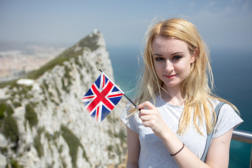Young woman holding a Union Jack with The Rock of Gibraltar in the background, indicating the dispute over its sovereignty and the effect of Brexit