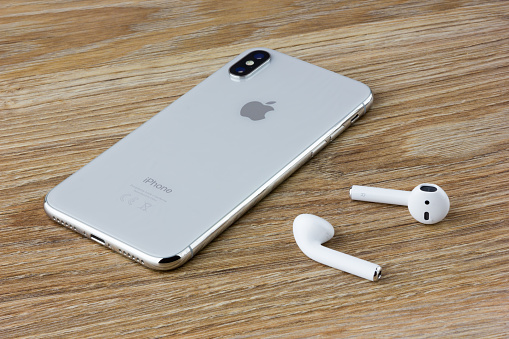 Rostov-on-Don, Russia - September 2018: The Iphone 10 lies on a wooden table next to the wireless headphones airpods from the Apple.
