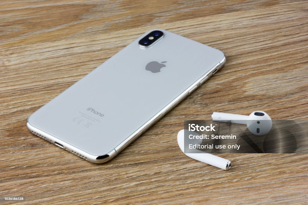 The Iphone 10 lies on a wooden table next to the wireless headphones airpods from the Apple. Rostov-on-Don, Russia - September 2018: The Iphone 10 lies on a wooden table next to the wireless headphones airpods from the Apple. Apple Computers Stock Photo
