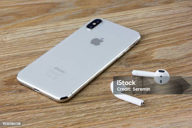 The Iphone 10 Lies On A Wooden Table Next To The Wireless Headphones Airpods From The Apple Stock Photo - Download Image Now