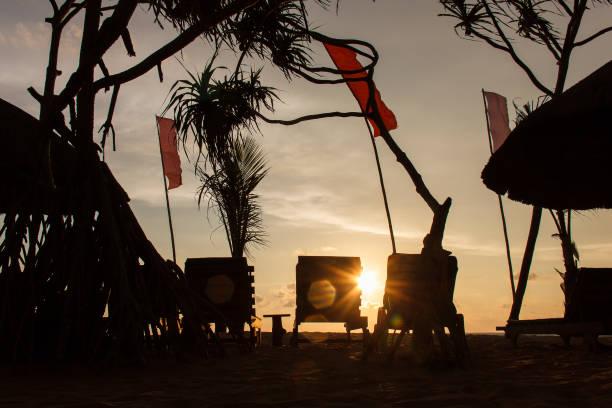 istock Three empty deck chair silhouettes at sunset beach, red flags waving, Thejan Beach Cabanas hotel, Bentota, Sri Lanka 1036190788