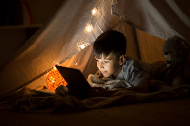 istock Little boy reading book on digital tablet at night 1036231776