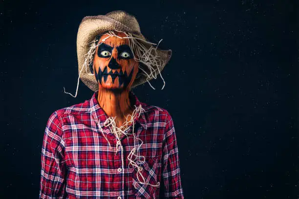 A person dressed as a creepy scarecrow with a pumpkin face.