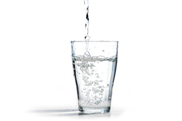 l'acqua viene versata in un bicchiere da bere, isolata su uno sfondo bianco con spazio di copia - bicchiere foto e immagini stock
