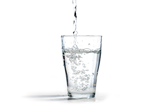 water is poured into a drinking glass, isolated on a white background with copy space