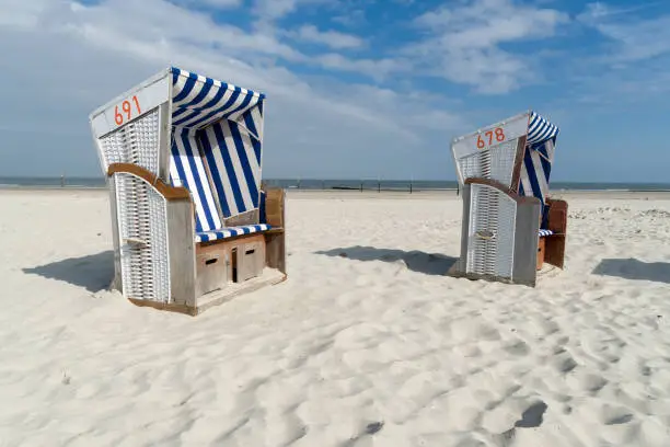Two roofed wicker beach chairs at the coastline of the German island Norderney in front of the ocean. Wide angle view