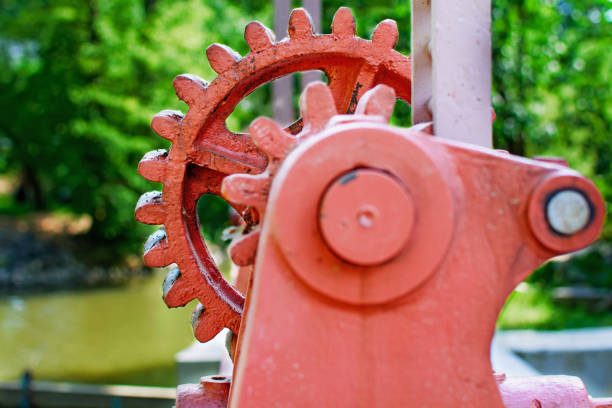 Close-up of a red metal gear on the floodgate. Mechanism to open the dam. Old toothed wheel on the river. Transfer to the opening of the dam. Old cogwheel