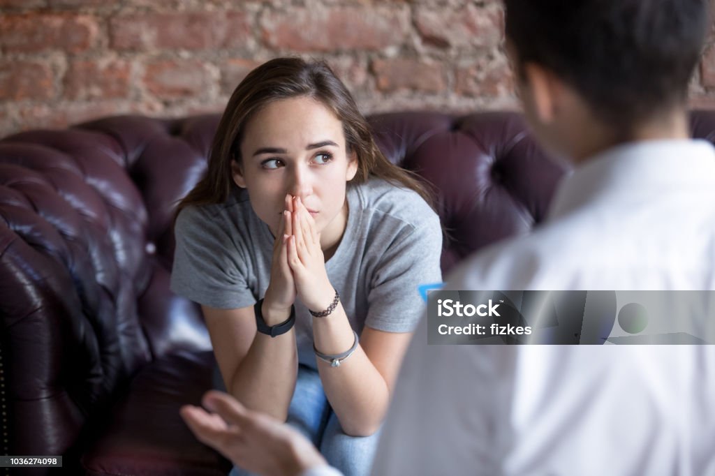 Unhappy young girl at the psychologist Young woman visiting therapist counselor. Girl feeling depressed, unhappy and hopeless, needs assistance. Serious disease, unwilling pregnancy, abort or death of loved one, addiction to drugs concept Teenager Stock Photo