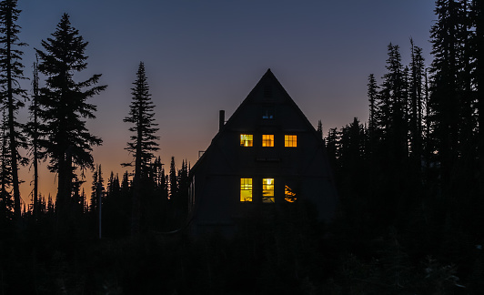 Wooden cabin in the woods at night; windows are lit