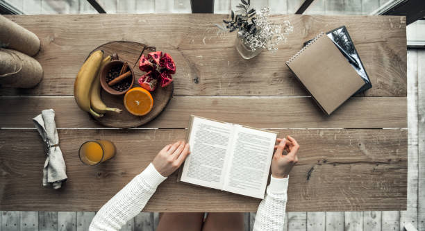 Top view of girl sitting at the wooden table and reading, cropped