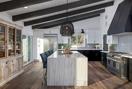 The interior of a large U-shaped kitchen with a wooden front and a large island. Stylish, cozy kitchen with appliances and plants with sun rays. View from the ceiling to threnderinge kitchen. 3d