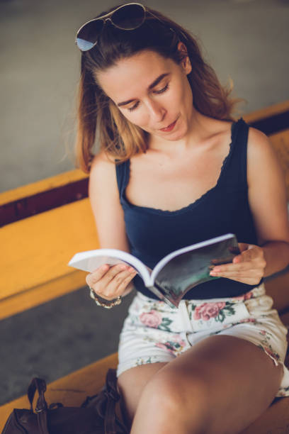 Young female student reads book on a bench downtown
