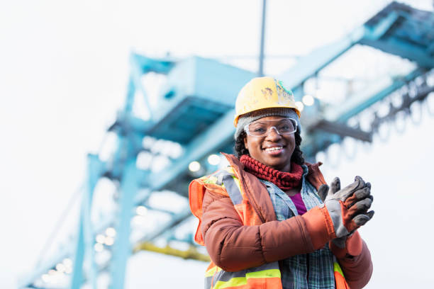 African-American woman working at shipping port A mid adult African-American woman in her 30s wearing a hard hat, safety vest and safety goggles, a dock worker working at a shipping port. A gantry crane is out of focus in the background. construction worker stock pictures, royalty-free photos & images