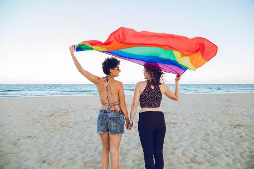 Girlfriends posing with rainbow flag by the sea