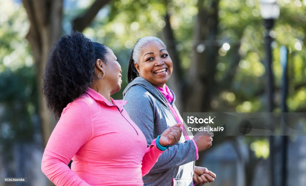 Mature African-American women in city, exercising Two African-American women exercising together in the city, jogging or power walking, laughing and conversing. Buildings and trees are out of focus in the background. The one in pink is in her 60s and her friend is in her 50s. Exercising Stock Photo