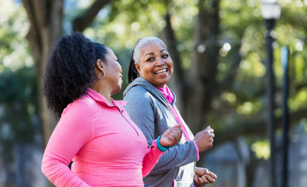 Mature African-American women in city, exercising Two African-American women exercising together in the city, jogging or power walking, laughing and conversing. Buildings and trees are out of focus in the background. The one in pink is in her 60s and her friend is in her 50s. power walking photos stock pictures, royalty-free photos & images