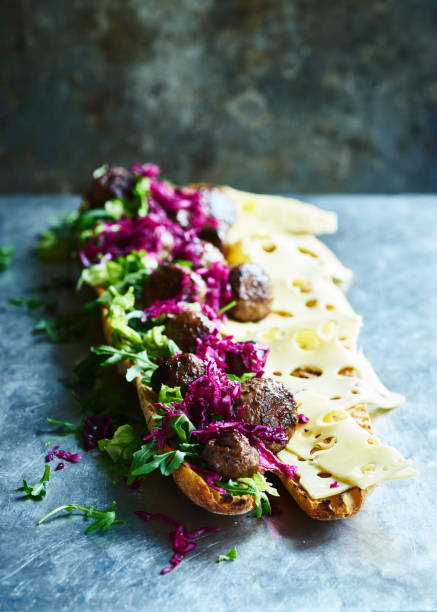 An open meatball sub sandwich with cheese, rocket salad and red cabbage on a metal surface