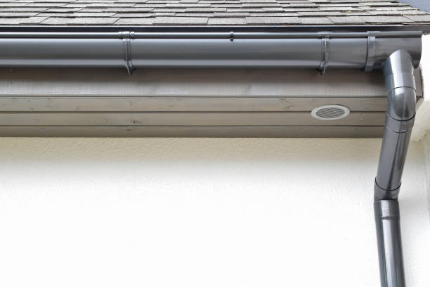Rain gutter Grey plastic rain gutter with drain downspout pipe installed on asphalt shingles roof wooden eaves with round ventilation grille with copy space for text on white facade. Home improvement concept. eaves stock pictures, royalty-free photos & images