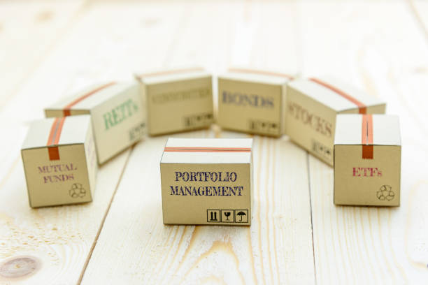 Portfolio and wealth management with risk diversification concept : Small paper cartons / boxes of financial instruments i.e ETFs, REITs, stocks, bonds, mutual funds and commodities, on a wood table.