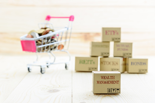 Long term sustainable and wealth management with risk diversification concept : Box printed with financial instrument / investment products i.e stocks, ETFs, bonds, REITs and coins in a shopping cart.