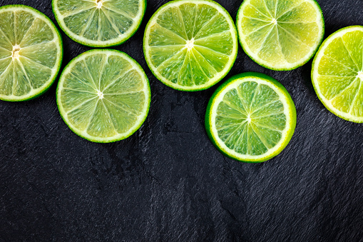 An overhead photo of many lime slices on a black background