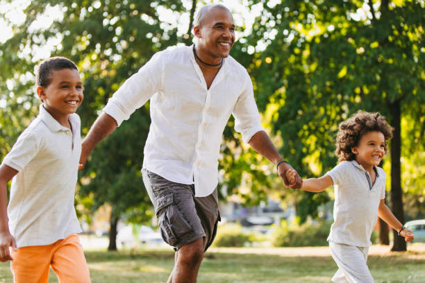 istock Two sons and their father holding hands and running in the park 1036606304