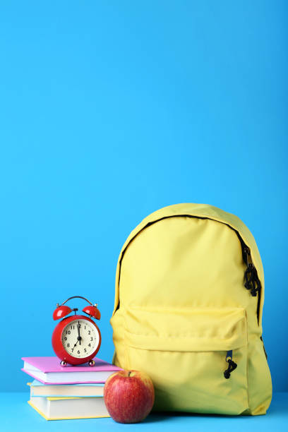 istock Yellow backpack with book and alarm clock on blue background 1036607036