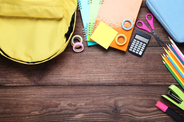 istock Yellow backpack with school supplies on brown wooden table 1036610210