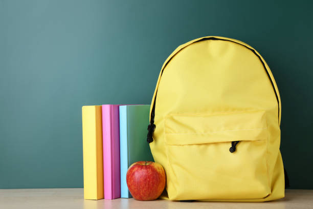 istock Yellow backpack with books and apple on green background 1036610378