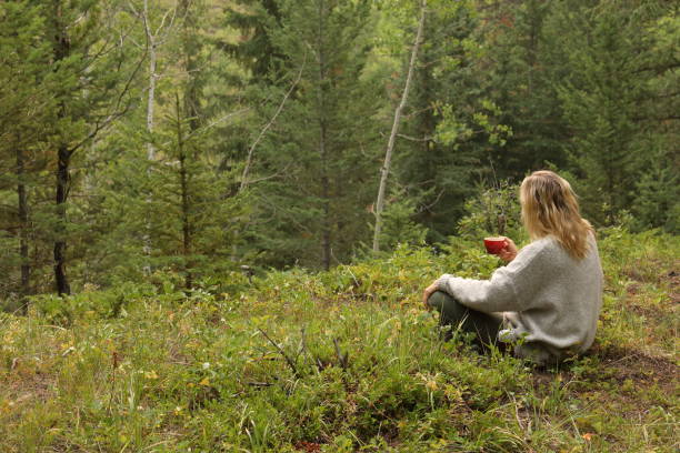 la donna beve caffè mattutino, mentre è seduta nel prato della foresta - footpath field nature contemplation foto e immagini stock