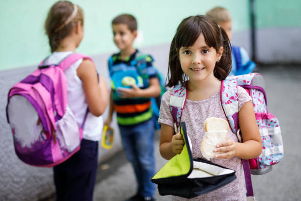 Little girl holding lunch box and eating sandwich Little girl holding lunch box and eating sandwich in a school yard food elementary student healthy eating schoolboy stock pictures, royalty-free photos & images