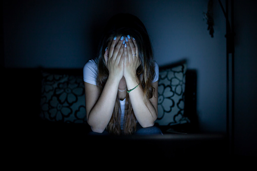 Girl sitting alone in dark room can't watch some scare scene on a laptop