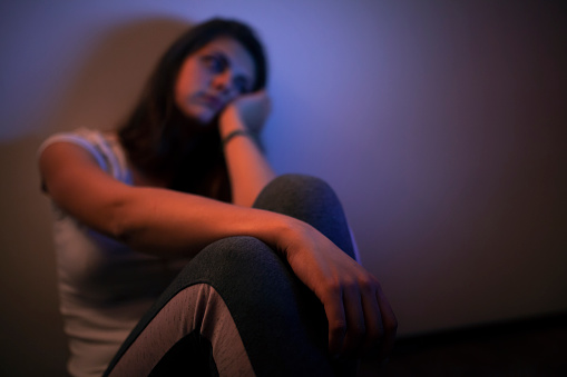 Depressed young woman sitting in the dark bedroom all alone