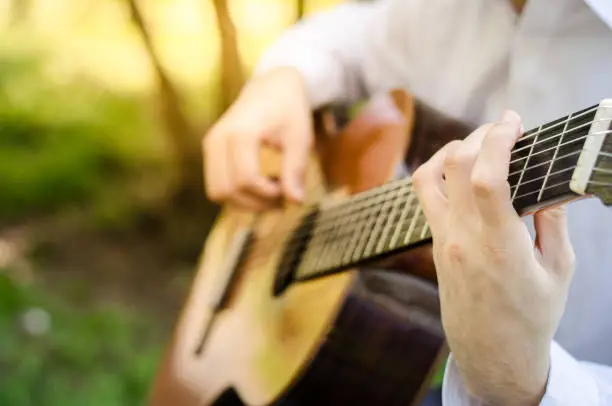 Close-up of the acoustic guitar played by a male guitarist in the park with warm sunlight. Music in the nature.